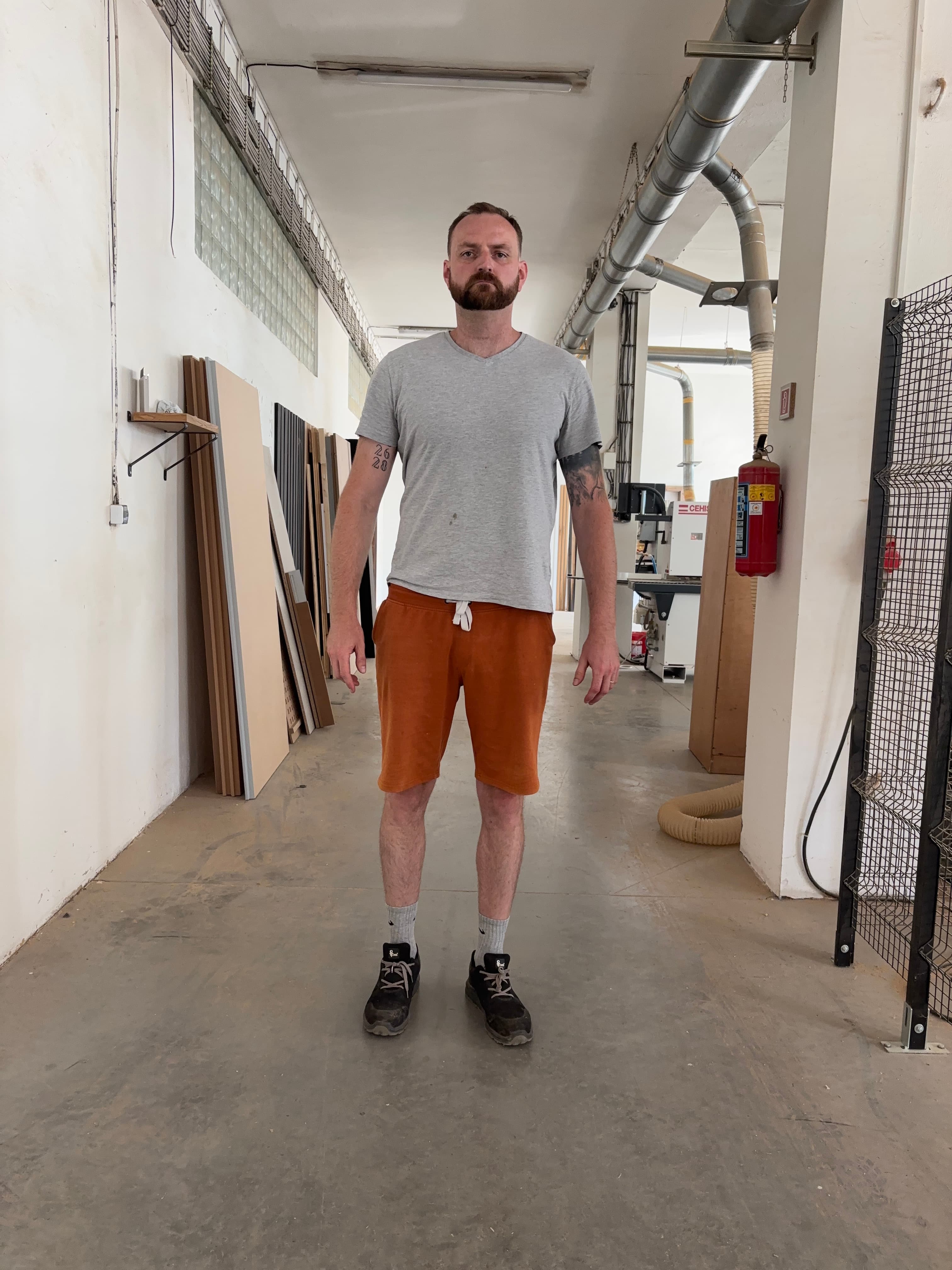 Tom standing in the workshop next to stacked panel offcuts